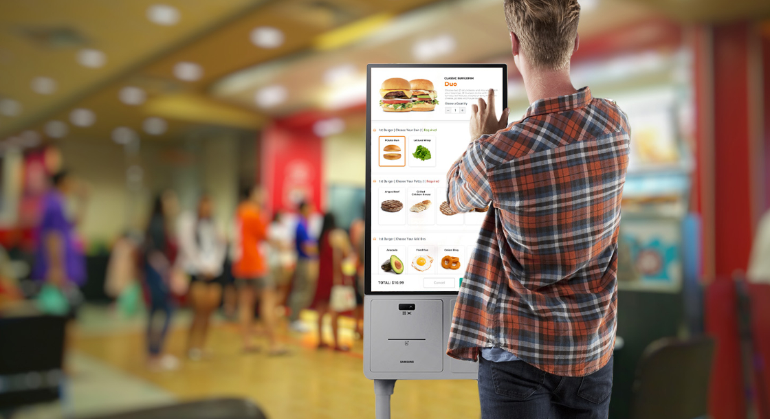 man in plaid button up shirt using samsung floor standing kiosk to order a burger