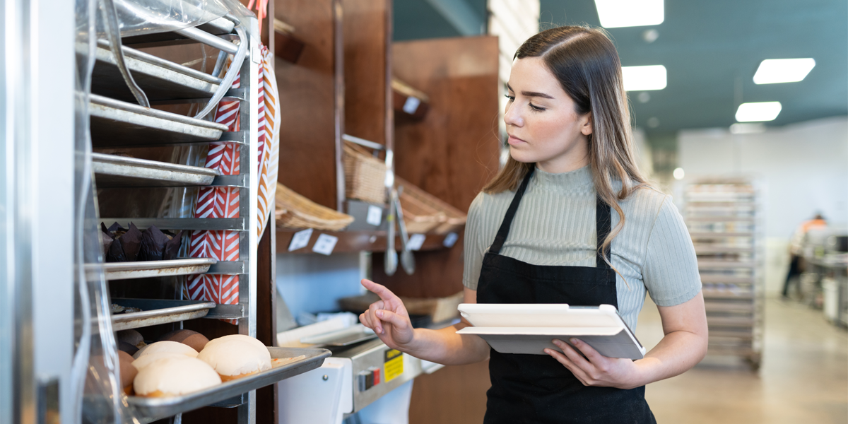 Woman In Kitchen Holding Tablet For Management Software